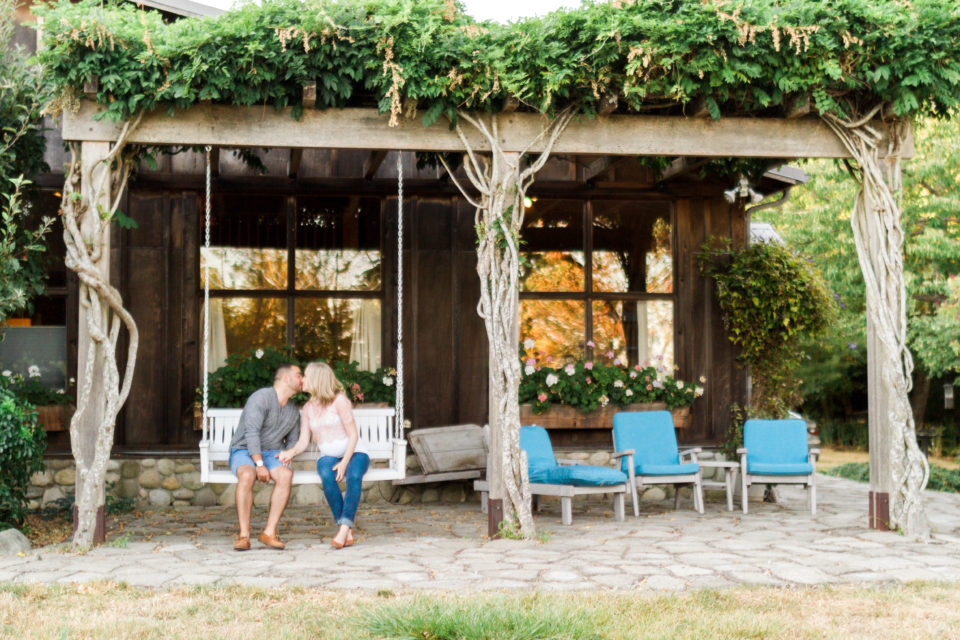 The couple kiss on a covered patio with gorgeous greenery growing around it