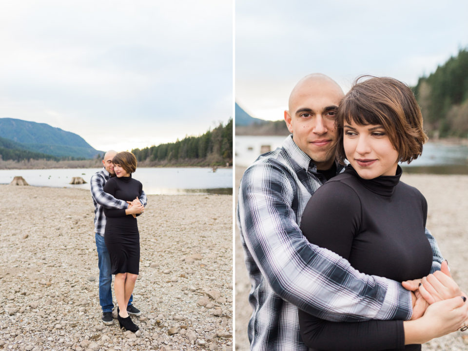A man lovingly squeezes a girl from behind as they stand in front of a lake