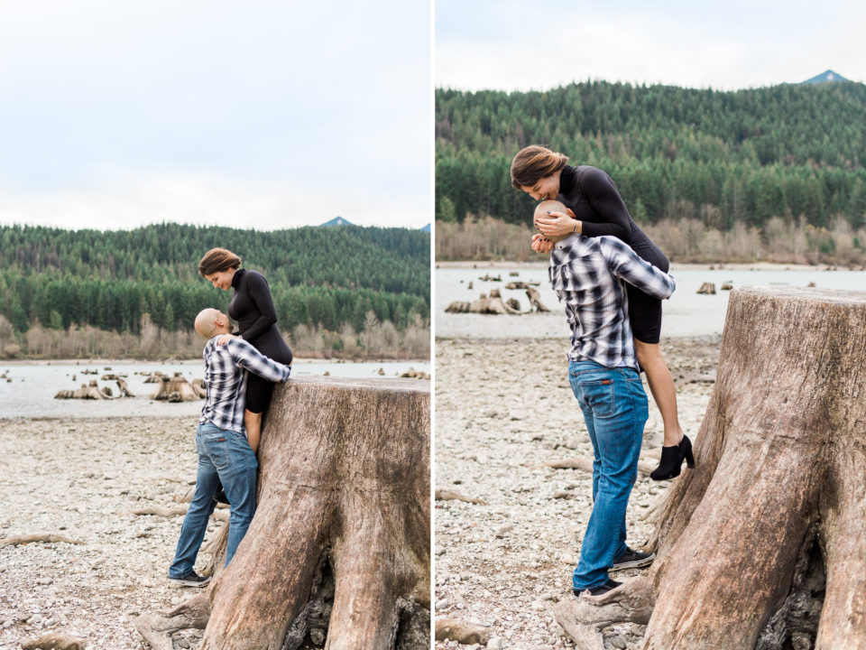 A man playfully helps his girlfriend off of a tall stump as she laughs
