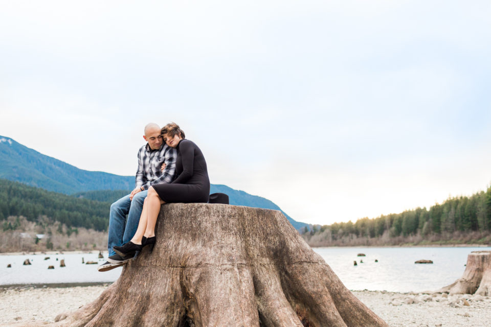 A young couple sit close together on a large tree stump