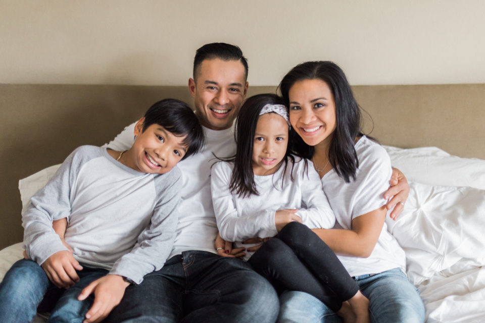 A family hugs each other and smiles at the camera during their in-home family session