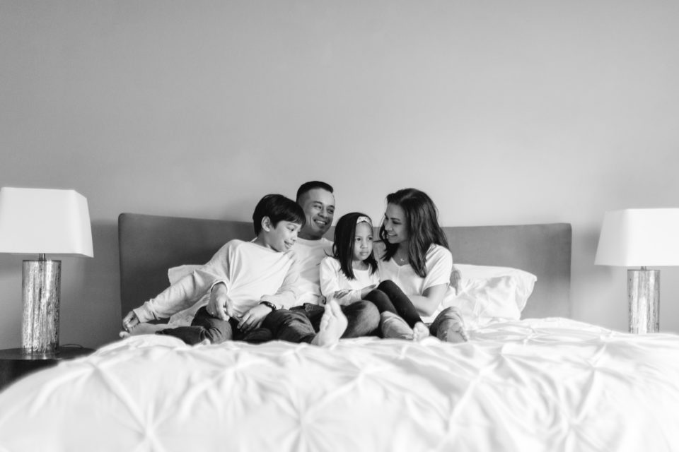 A family sits close together and talks on their bed