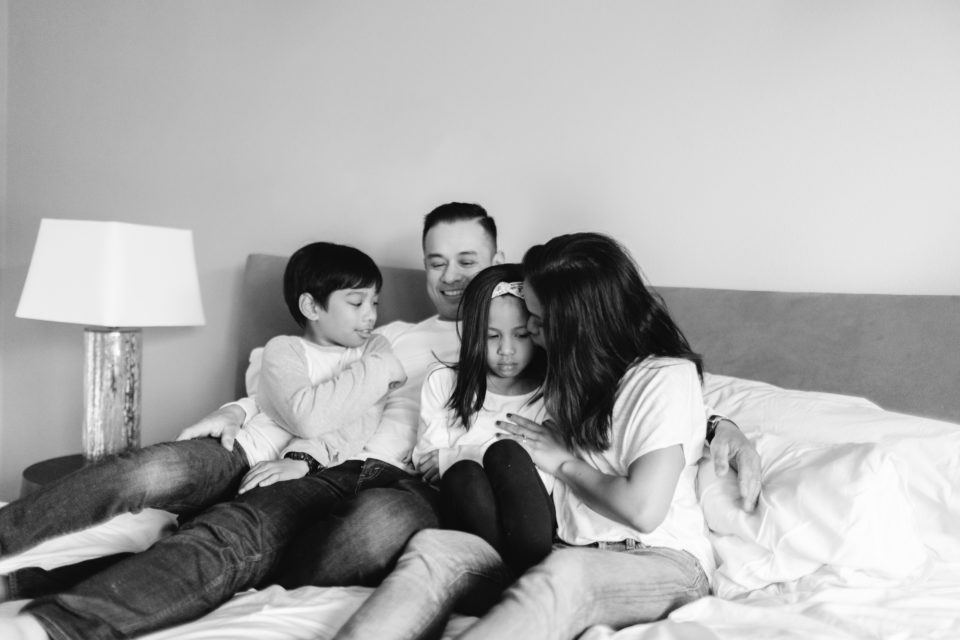 A family of four wearing white snuggles together on a bed