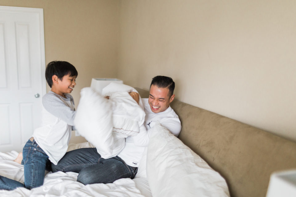 A boy has a pillow fight with his dad and hits him in the face