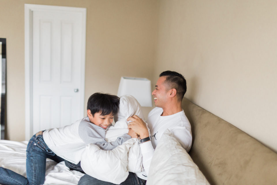 A dad laughs as his son tackles him with a pillow 