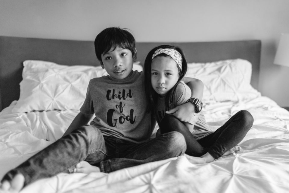 A little sister makes a sour face as her brother wraps his arms around her