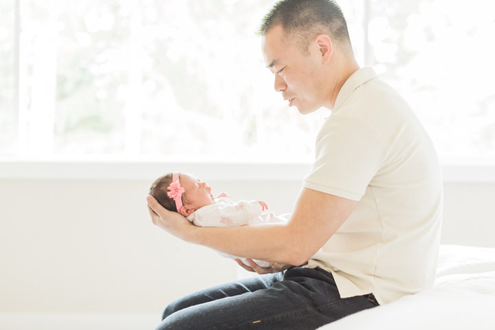 Dad holds his infant daughter in his hands in a light and airy room