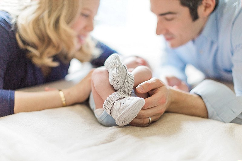 Tiny boots cover the feet of a new baby as he lays in between his smiling parents