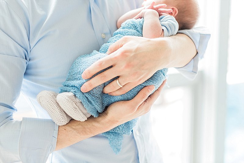 A man holds his new sleeping son in his arms and they are both wearing blue