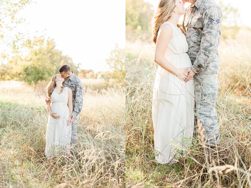 An expectant couple kiss in a field of golden grass