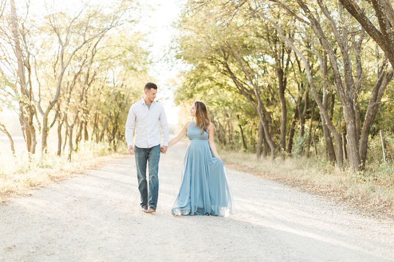The soon to be parents walk hand in hand down a tree lined road