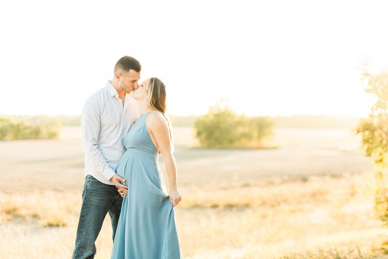 A gorgeous pregnant couple kiss as they stand in farm land