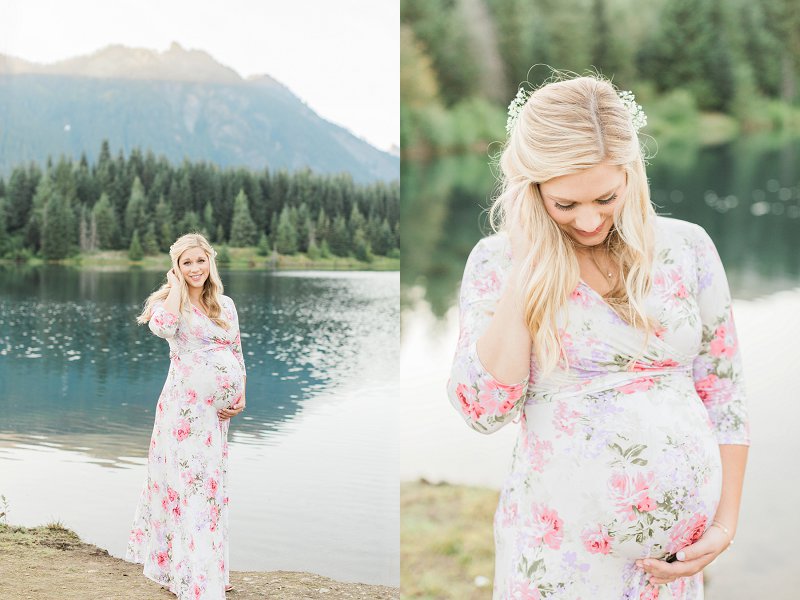 A blonde woman wearing a pink and white dress cradles her baby bump and smiles happily