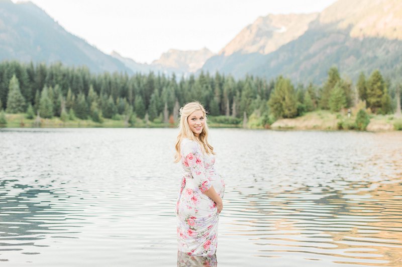 A beautiful view of an expectant woman standing in a lake with the stunning mountains behind her