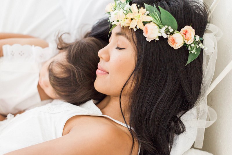 A Mother wearing a colorful flower crown closes her eyes as she holds her child close