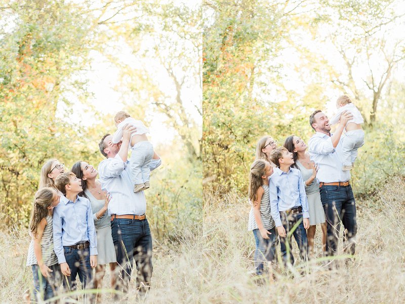 A baby boy is thrown high in the air by his Dad as their family looks on and smiles