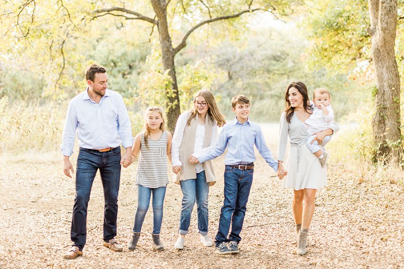 The sweet family walk along the leafy path in a park in Dallas during their photo session