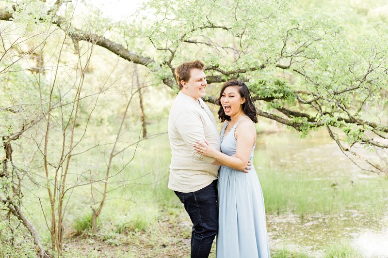 The couple laughs out loud together as they stand in front of a small pond
