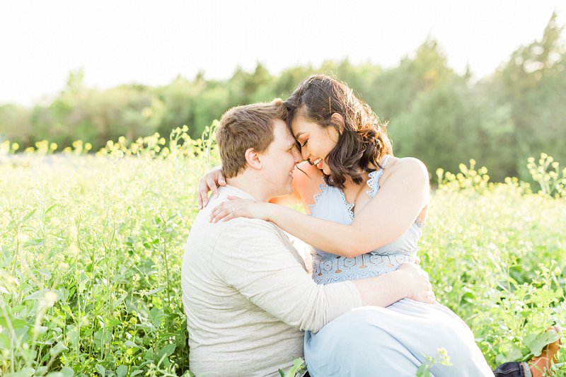 A couple leans in to kiss each other as they sit in a field of yellow flowers