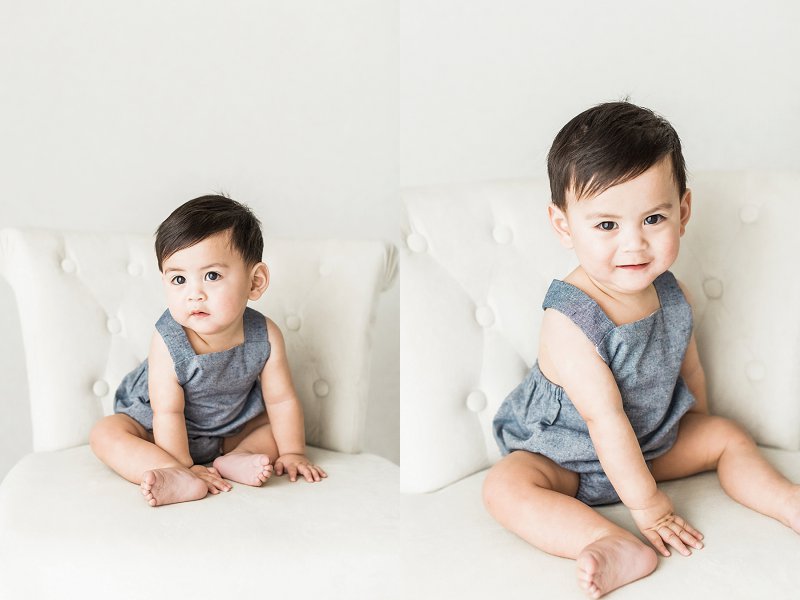 A sweet baby sits and poses himself in his denim romper in an all white studio