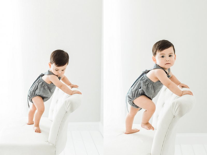 Baby stands on the chair and holds the back while he looks around the room