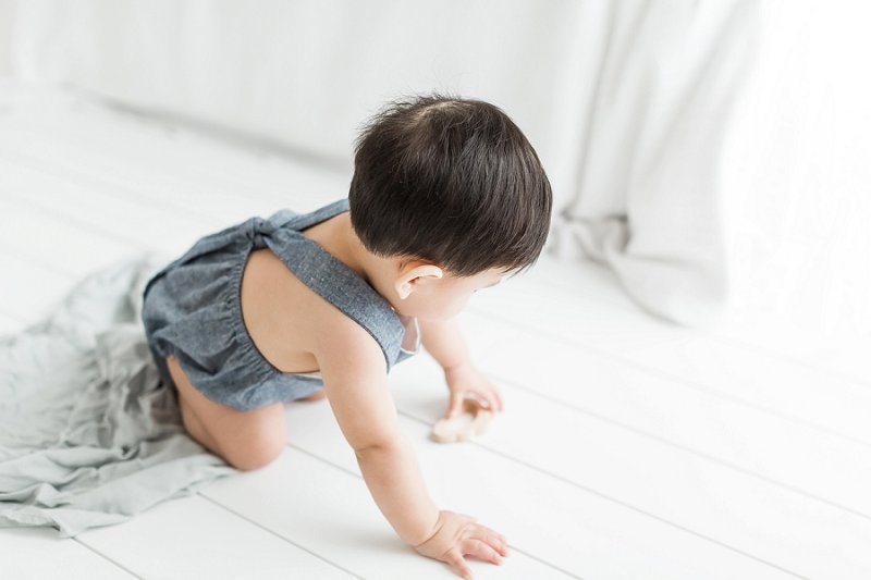 A little one plays with an organic wooden cloud shaped toy as he crawls along the floor