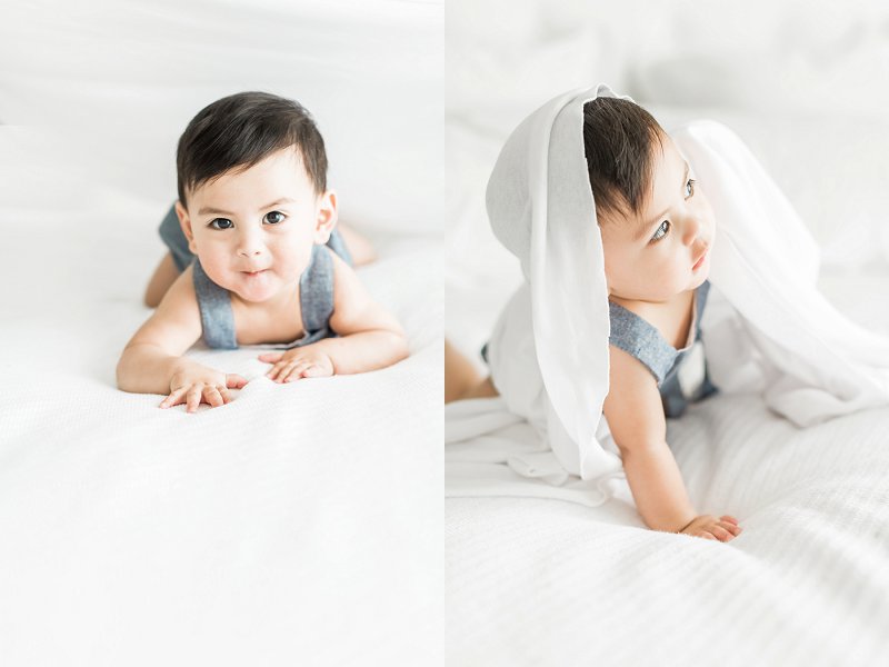 A soft white cloth is draped over baby boy's head and he grabs it and yanks it off his head