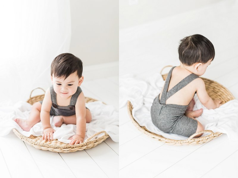A curious little boy plays with the basket he’s sitting in in an all white studio