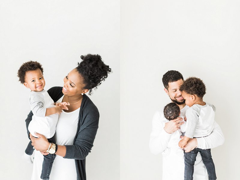 Both parents stand against the white backdrop and encourage their oldest son to interact with this little brother 