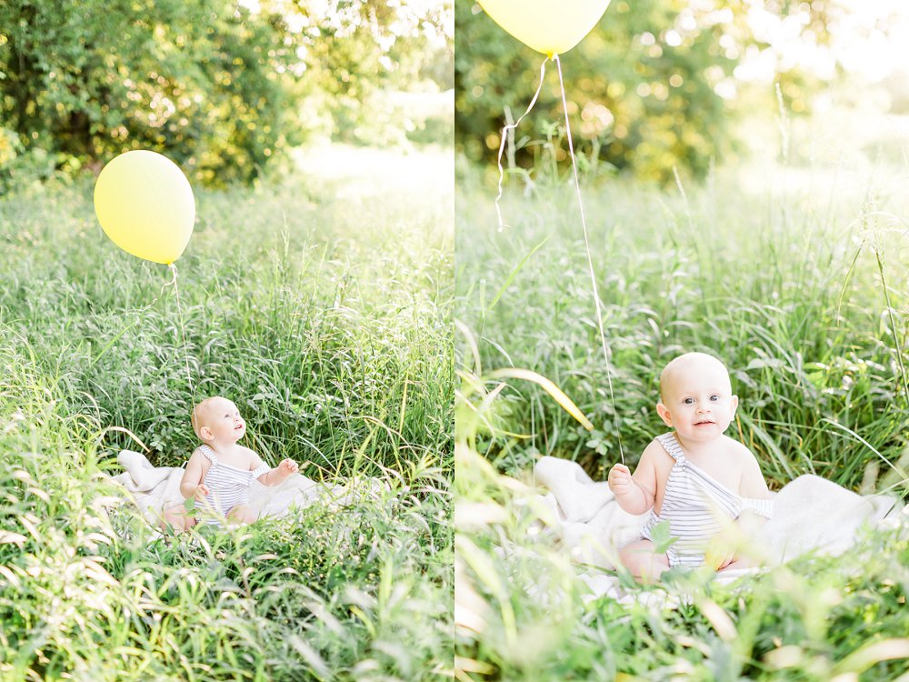 the one year old sits in a field of tall grass and plays with his yellow balloon 
