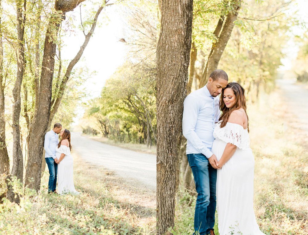 A pulled back shot of the pregnant couple kissing each other underneath the canopy of the tall green trees