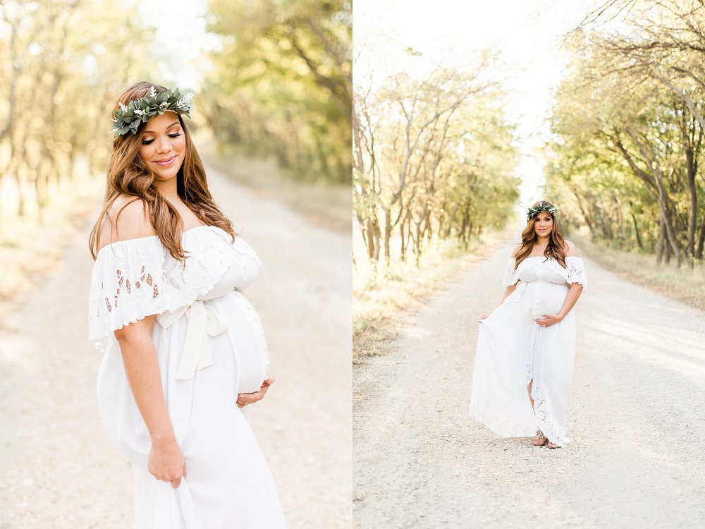 A brunette pregnant woman wearing a flower crown made of greenery walks on the dirt path and smiles