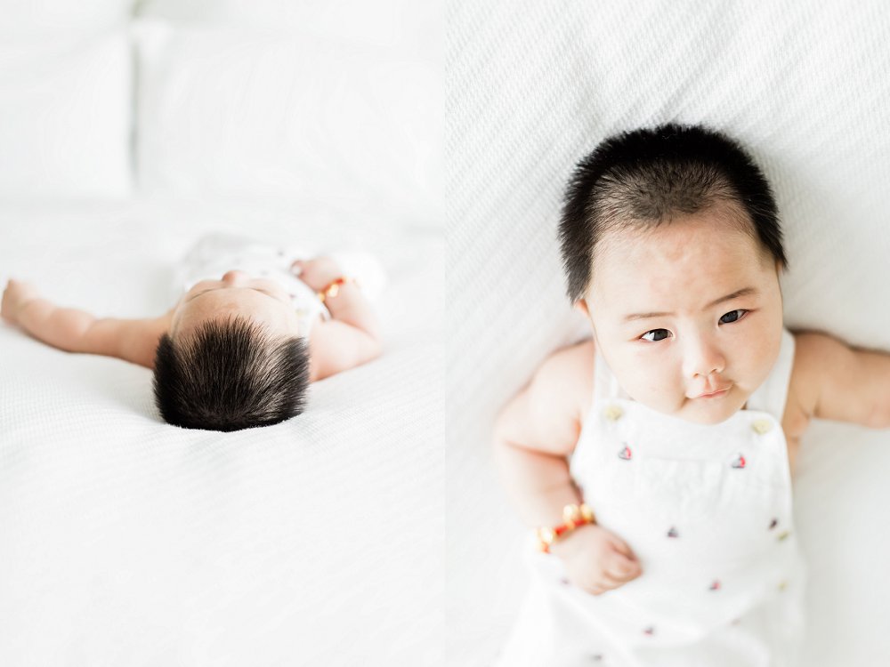 A baby with lots of dark hair looks straight at the camera as he lays on a white blanket