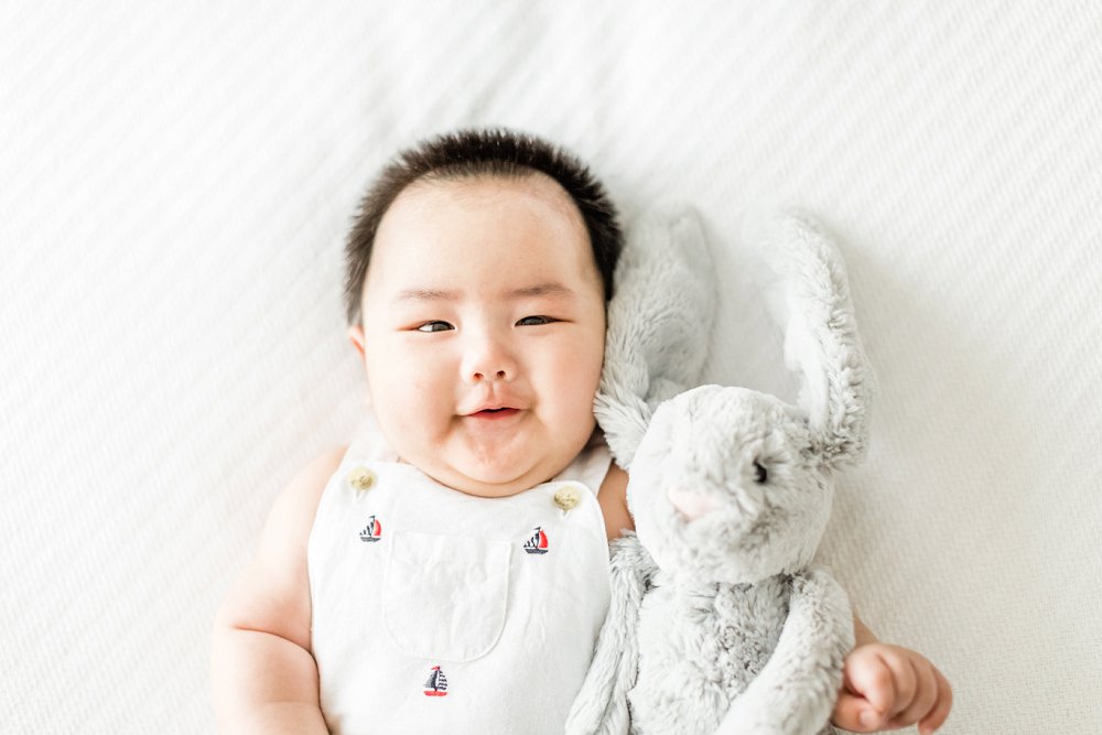 The little boy smiles up at the camera as he holds his grey stuffed bunny