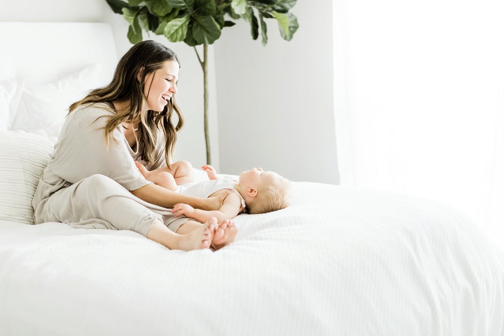 A mother and baby play together in a light and airy studio on a white bed