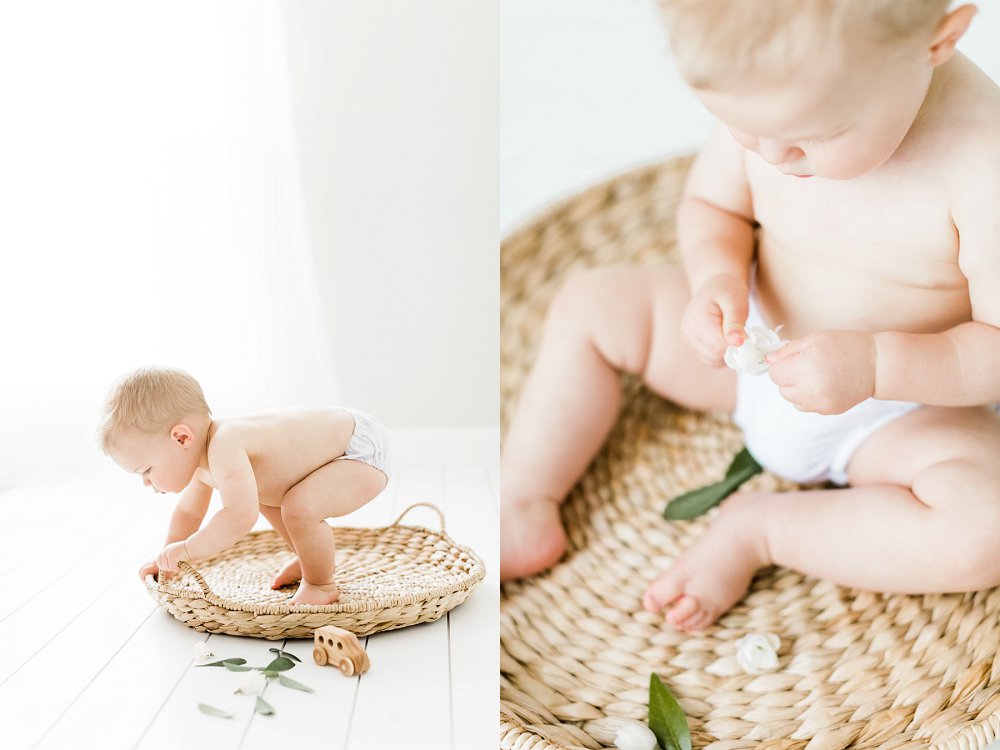 A candid photo of a baby playing with leaves and flowers in a dallas all white studio