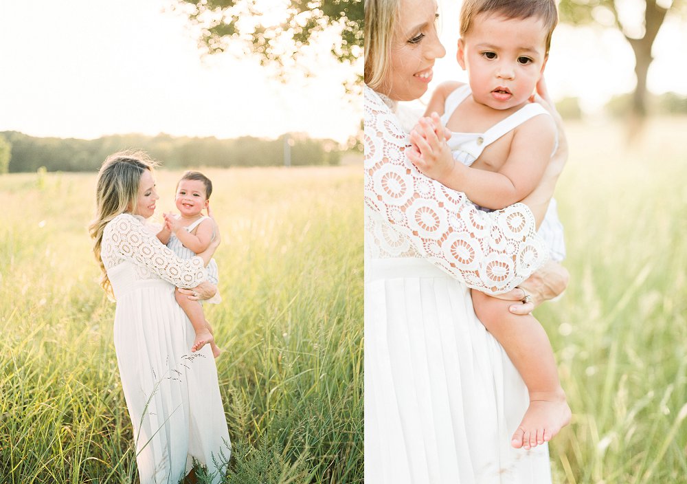 A mother wearing a lace sleeved white dress holds her son on top of her growing baby bump