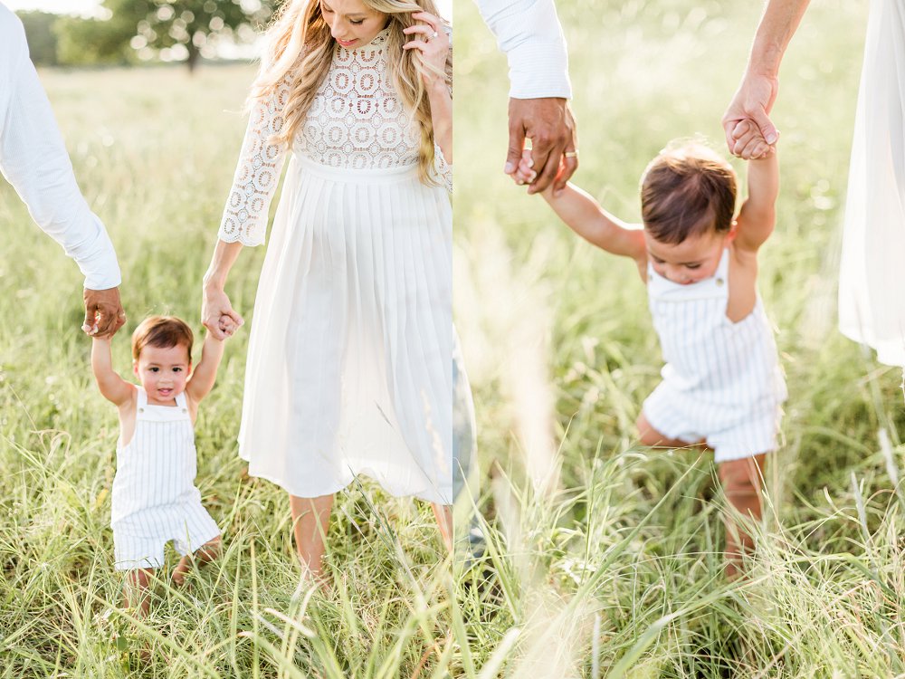 The toddler holds each of his parents hands and walks through the tall green grass