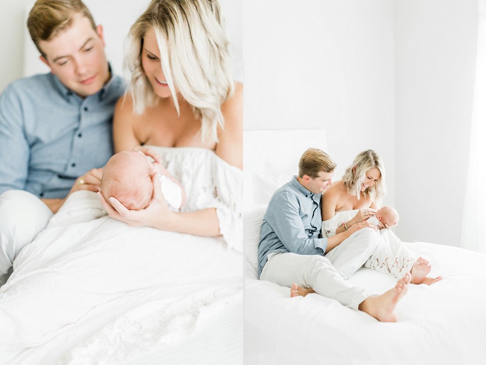 Dad and Mom sit on a bed and smile at newborn baby