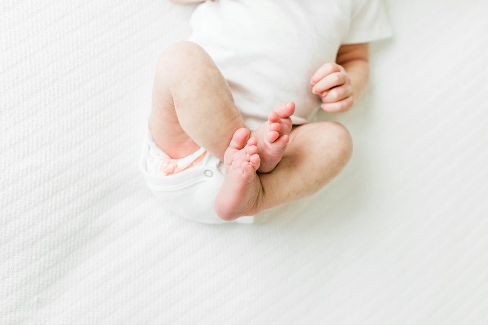 Newborn baby wearing white onesie laying on a white bed