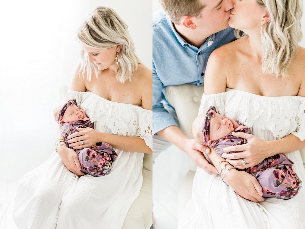 Mom and Dad kiss while holding newborn baby girl