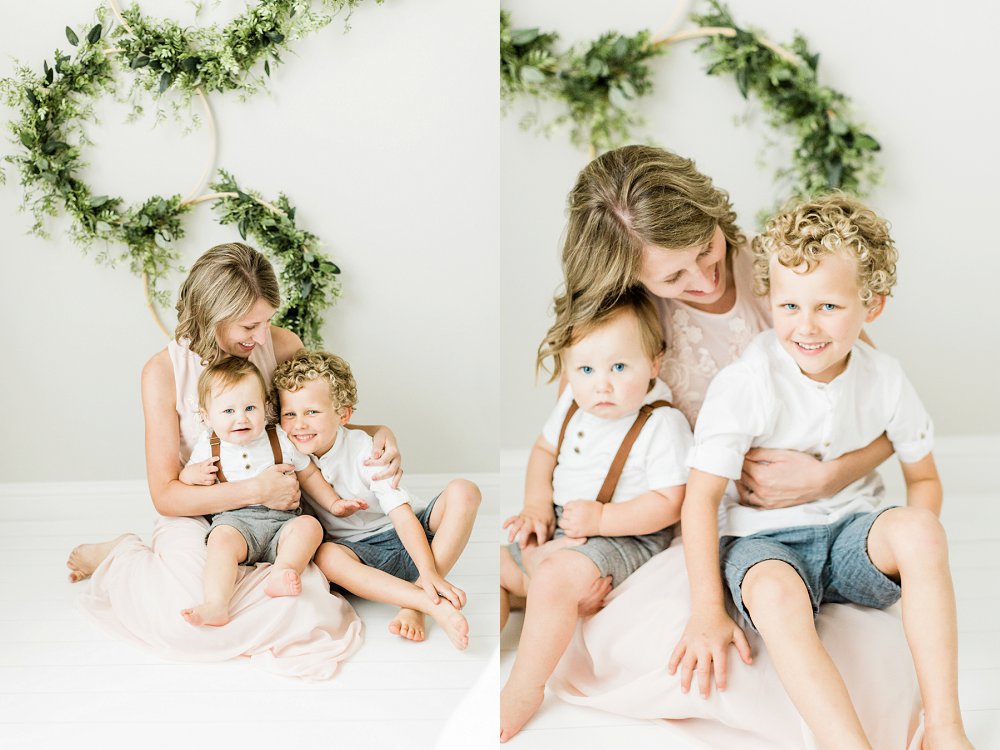 Mom hugging sons in white studio with greenery