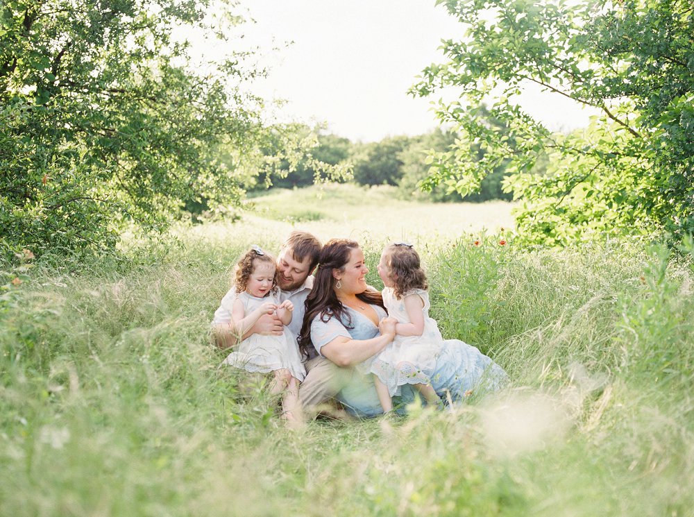 A family lounges together in the tall grass and quietly plays together