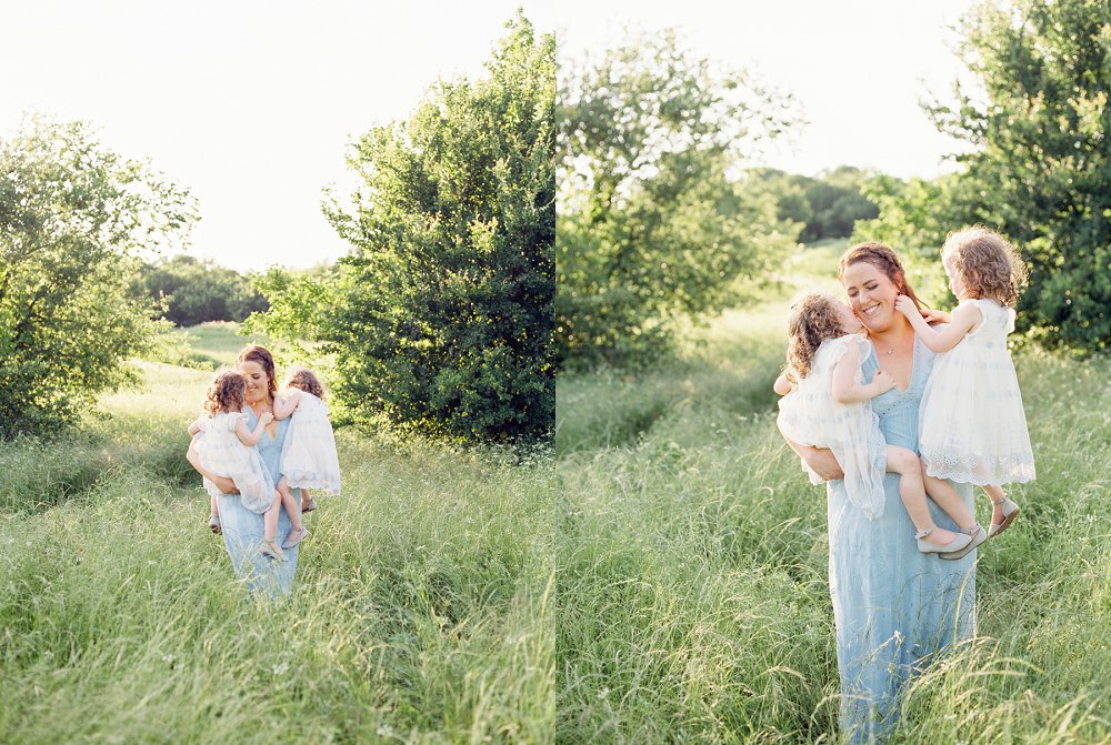 A Mom wearing a long lace blue dress walks through a field with her twin daughters
