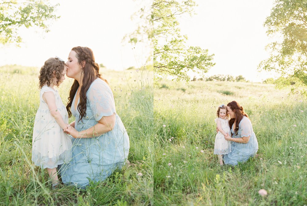 Mom gives a sweet kiss to her daughter on the forehead as they sit together in the grass